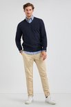 Man met marineblauwe V-hals trui over een lichtblauw overhemd en beige broek.