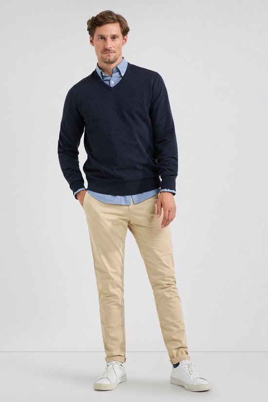 Man met marineblauwe V-hals trui over een lichtblauw overhemd en beige broek.