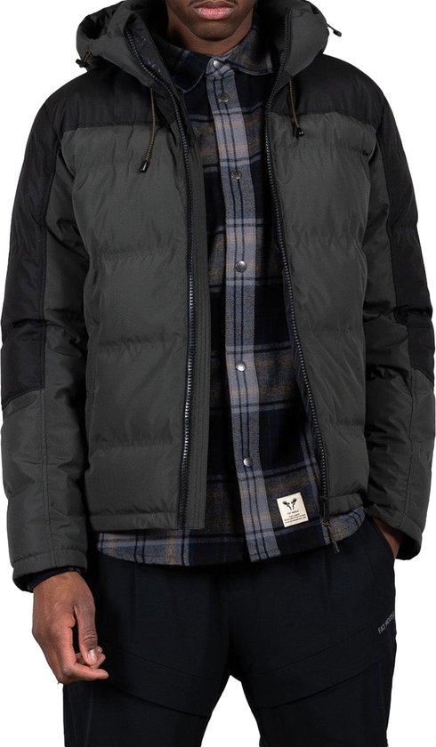 Man draagt donkergrijze en zwarte winterjas met capuchon, geruite blouse en zwarte broek.