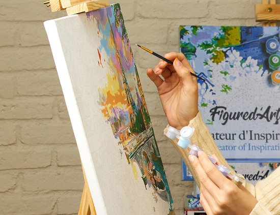 Vrouw schildert een landschap met gekleurde gebouwen en water met acrylverf op canvas. Links 'Figured'Art'.