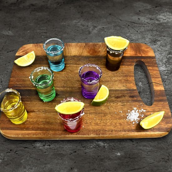 Houten plank met zes gekleurde shotglazen met zoutranden, citroenpartjes en witte kruimels.