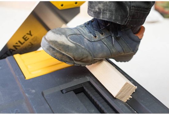 Voet met werkschoen op een stuk hout dat op een zwarte Stanley gereedschapskoffer ligt.