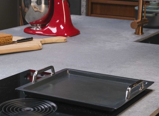 Gietijzeren teppanyaki plaat met zilverkleurige handvatten op een inductiekookplaat.