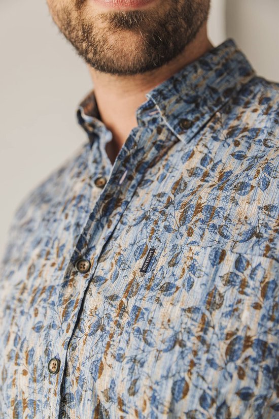 Close-up van de kraag van een man in een blauw overhemd met bruine bladprint.