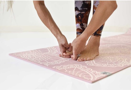 Een persoon met een abstracte legging die een roze yogamat met wit bloemenpatroon vasthoudt.
