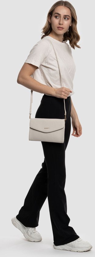 Crèmekleurige lederen schoudertas met goudkleurig logo, gedragen door een model met een zwarte broek.
