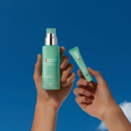 Handen houden een BIOTHERM HOMME Aquapower Comfort Gel flesje en een oogcrème vast, tegen een blauwe hemel