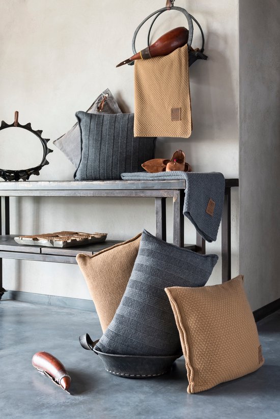 Coussins et plaids tricotés gris foncé et marron, certains à rayures verticales, sur une étagère en métal.