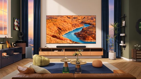 Royale woonkamer met grote tv waarop natuurschap te zien is, soundbar en grijze subwoofer.