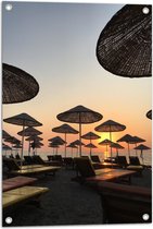 WallClassics - Tuinposter – Ligbedden met Rieten Parasols aan het Strand in de Avondzon - 50x75 cm Foto op Tuinposter (wanddecoratie voor buiten en binnen)
