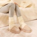 Model draagt beige suède pantoffels met dikke zool en crèmekleurige imitatiebontvoering bij grijze legging en sokken.