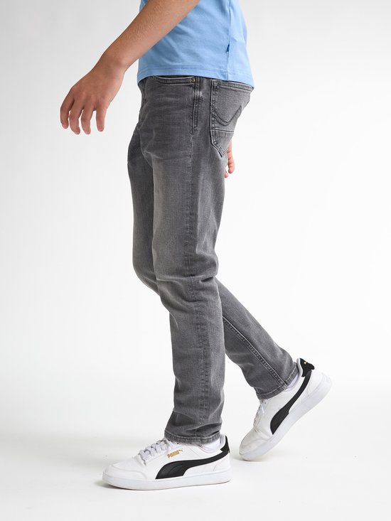 Jongen draagt een grijze Petrol Industries jeans met regular tapered fit, gecombineerd met een lichtblauw shirt en witte Puma sneakers.