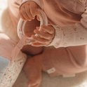 Babyhandjes die een doorzichtige ring vasthouden, naast een zacht speelgoed. Baby draagt roze kleding.