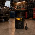 Zwarte en gele 3kW verwarming met handvat, staat op garagevloer naast auto.