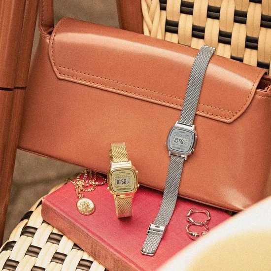 Goudkleurig en zilverkleurig Casio digitaal horloge met mesh-band op een rood boek voor een bruine tas.