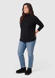 Zijaanzicht van een vrouw in een zwarte coltrui met lange mouwen, blauwe jeans en zwarte instappers.