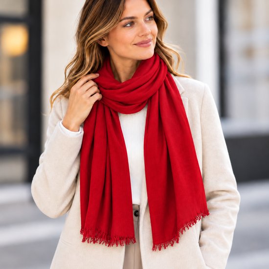 Femme portant une écharpe rouge vif avec des franges sur un manteau beige.