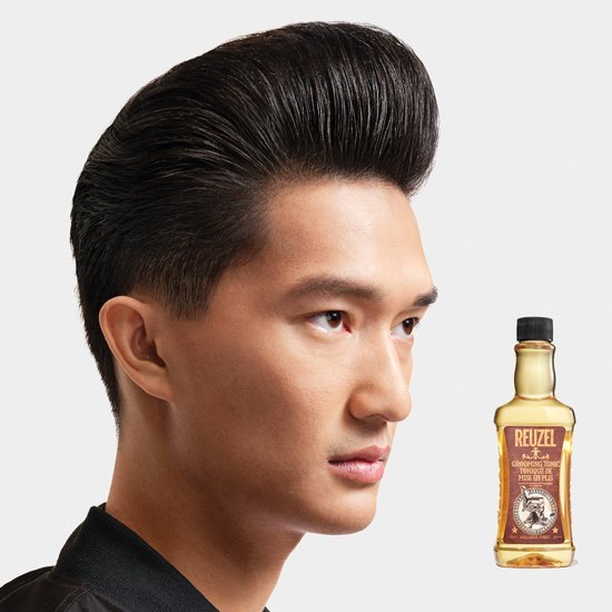 Zijaanzicht van een man met gestyled zwart haar in kuifmodel, naast een fles Reuzel Grooming Tonic.