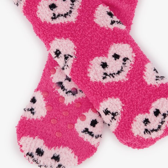 Detailopname van roze huissokken met een patroon van lachende hartjes en roze antislipnopjes op de onderkant.