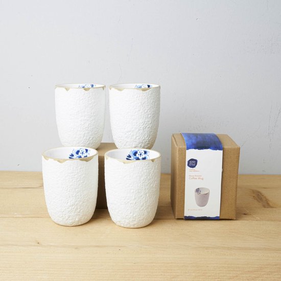 Vier witte koffiemokken met textuur, blauw bloesemmotief binnenin en bruine rand, naast een bruine doos.
