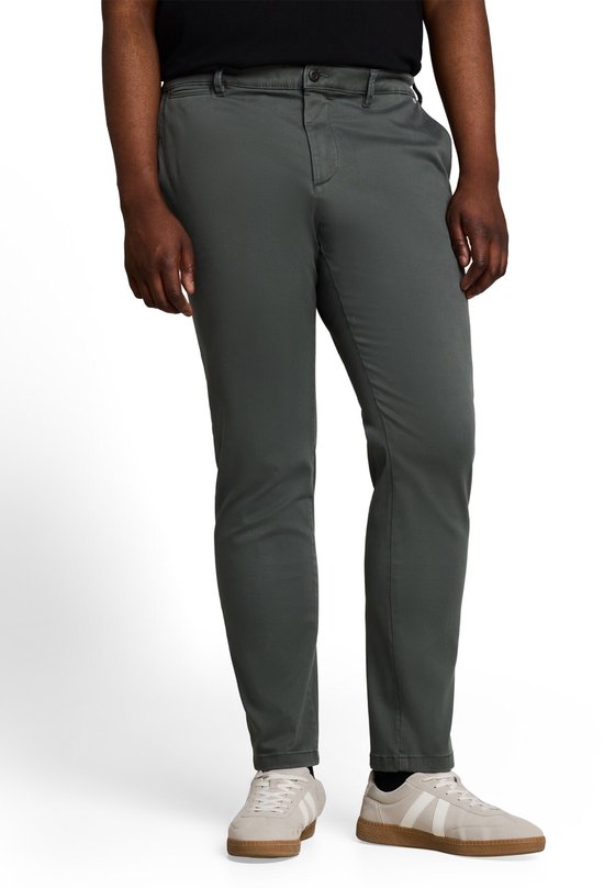 Donkergroene chino met normale pasvorm, gedragen door een man met een zwarte top en witte sneakers.