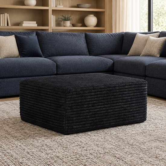 Zwarte ribfluwelen hocker voor een donkerblauwe bank in een woonkamer.