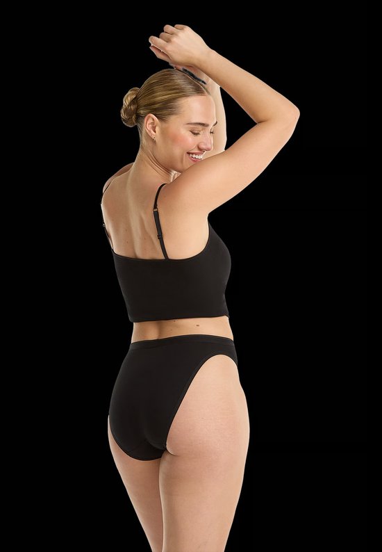 Model draagt een zwart hemdje en bijpassende zwarte slip, gezien vanaf de rug met opgeheven armen.