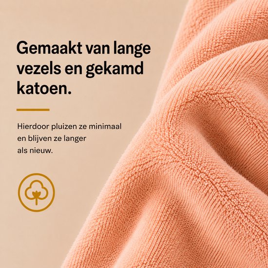 Close-up van zalmroze handdoekstof. Tekst: Gemaakt van lange vezels en gekamd katoen voor minder pluizen.