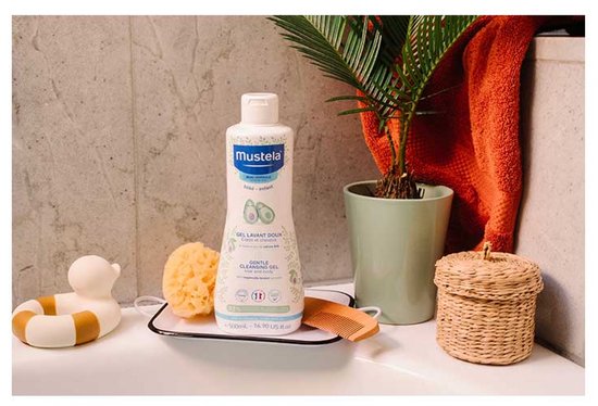 Mustela milde reinigingsgel voor baby's en kinderen, met avocado-illustraties, op een wastafel met badspeelgoed.