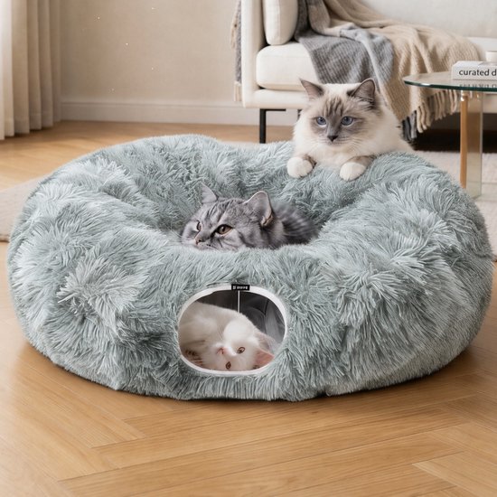 Drie katten in een rond lichtgrijs pluche kattenbed met een tunnelvormige opening.