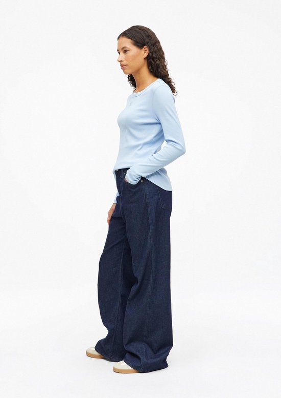 Zijaanzicht van model in lichtblauw geribbeld shirt en donkere jeans met wijde pijpen.