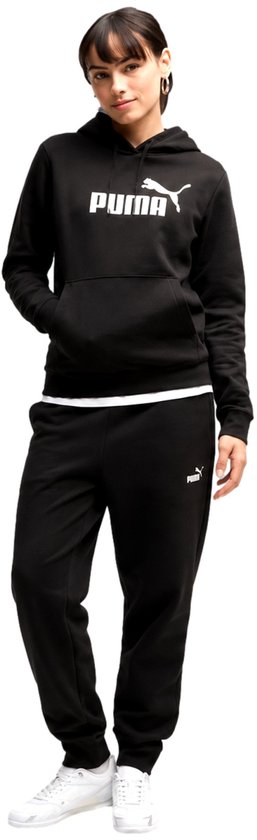 Model in een zwarte Puma hoodie en bijpassende joggingbroek, met de hand in de zak van de hoodie.