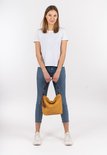 Model in wit T-shirt en spijkerbroek met een mosterdgele schoudertas met kwastjes.