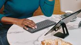 Vrouw met donkere huid met een groene trui typt op een donkergrijs Logitech Keys-to-Go 2 toetsenbord naast een tablet en gebak.