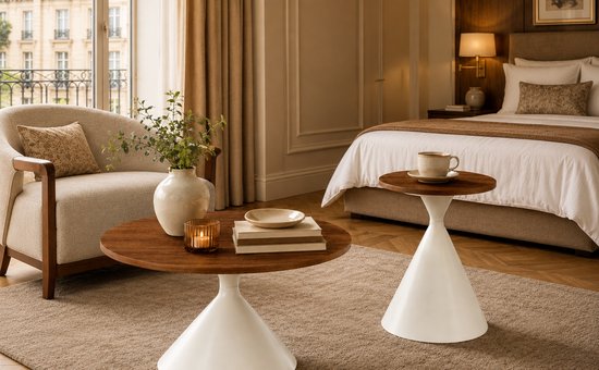 Ronde salontafel met walnoothouten blad en crèmewitte conische voet, naast een fauteuil en een bijzettafel.