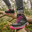 Zwarte hoge wandelschoenen met roze veters tijdens het wandelen op een omgevallen boomstam in het bos.