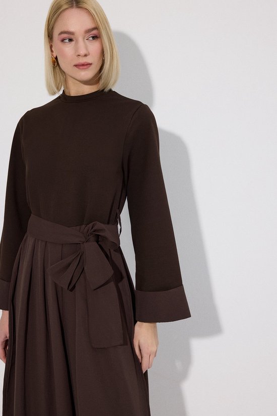 Close-up van een donkerbruine jumpsuit met strikceintuur en opgerolde mouwboorden.