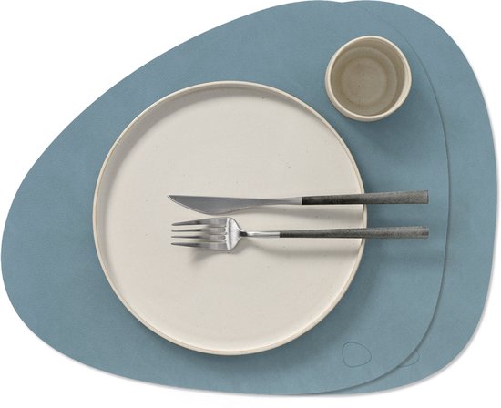 Un set de table bleu clair de forme incurvée, avec une assiette, des couverts et une tasse dessus.