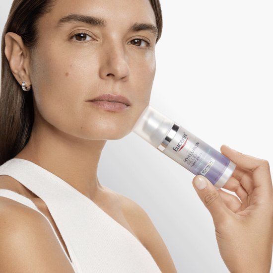 Vrouw met witte top die een Eucerin Hyaluron-Filler + Longevity nachtcrème flesje vasthoudt.