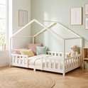Lit maison blanc avec barreaux, décoré de coussins colorés et d'un ours en peluche.
