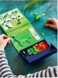 Kind bouwt groene dinosaurus met Plus-Plus bouwstenen, naast activity pad met instructies en bakje met stenen.