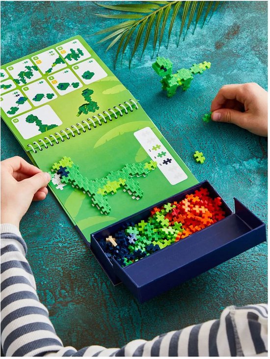 Kind bouwt groene dinosaurus met Plus-Plus bouwstenen, naast activity pad met instructies en bakje met stenen.