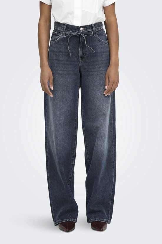 Donkerblauwe wijde jeans met strikceintuur. Model staat op witte achtergrond.
