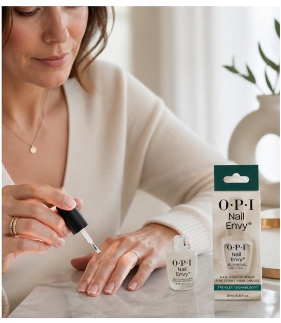 Vrouw met beige trui en ringen brengt O.P.I. Nail Envy aan op haar nagels.