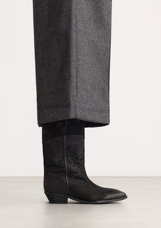 Model draagt zwarte nubuck cowboylaarzen onder een grijze broek.