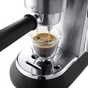 Zilverkleurige De'Longhi espressomachine met zwarte handgreep, die een espresso schenkt in een glazen kopje.