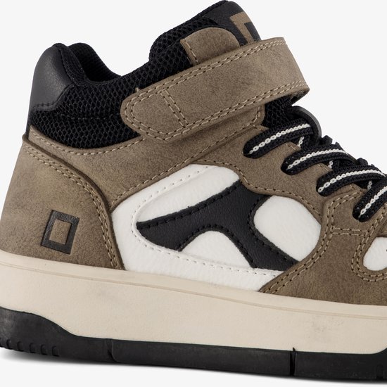 Detail van bruine hoge sneaker met witte en zwarte logo's, klittenbandsluiting.