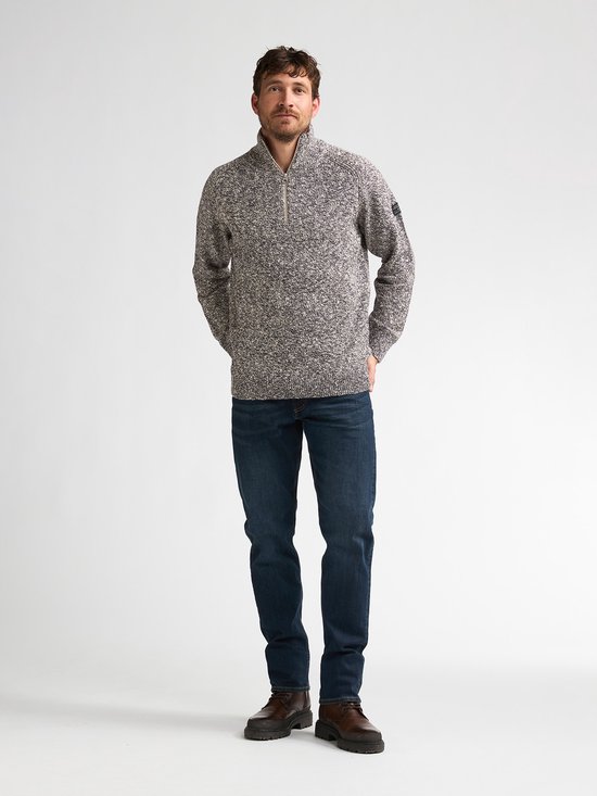 Man met gemêleerde blauw-witte trui met rits en donkere spijkerbroek.