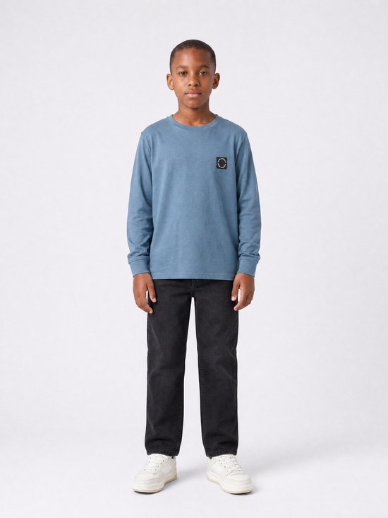 Jongen in blauw longsleeve T-shirt met borstlogo en zwarte jeans.