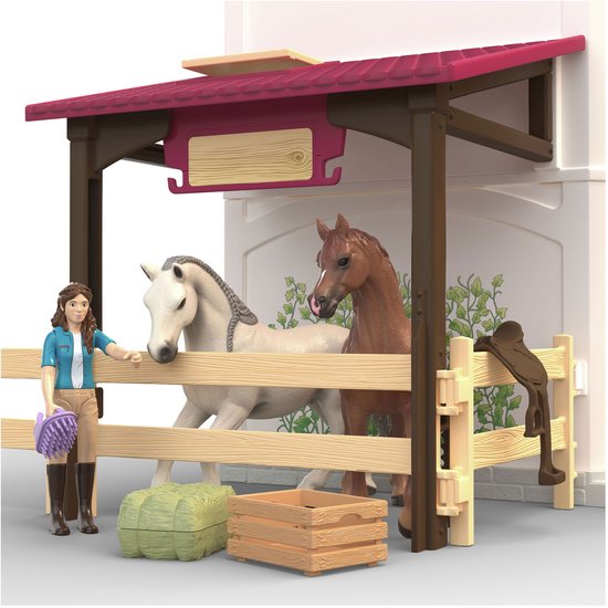 Paardenstal met houten hek, twee paarden, een meisje met borstel en hooibaal.